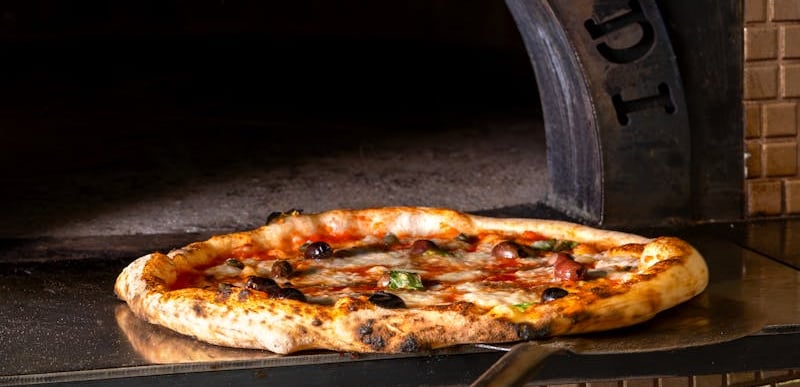 Pizza artigianale con olive appena sfornata dal forno a legna di AndrèsRosa Pizzeria ad Alseno
