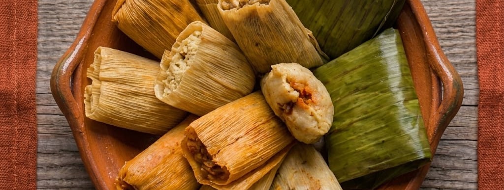 Variedad de tamales tradicionales mexicanos envueltos en hojas de maíz y hojas de plátano, servidos 