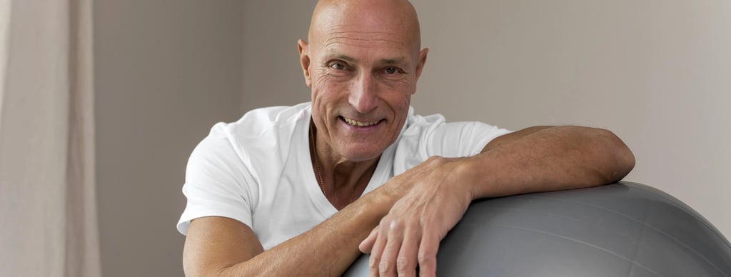 Homem careca sentado no chao ao lado de uma bola de pilates