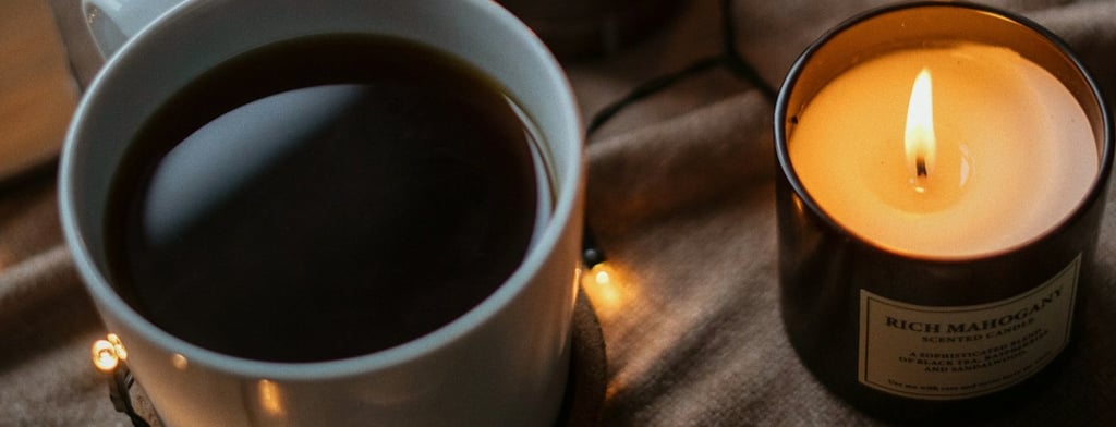 Taza de café caliente rodeada de velas y luces cálidas, evocando bienestar, calma y el ritual person
