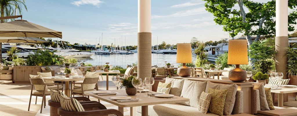 Luxury waterfront outdoor restaurant with elegant table settings and views of yachts in the harbor. 