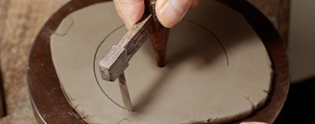 hand holding a wooden tool drawing circles on a clay slab