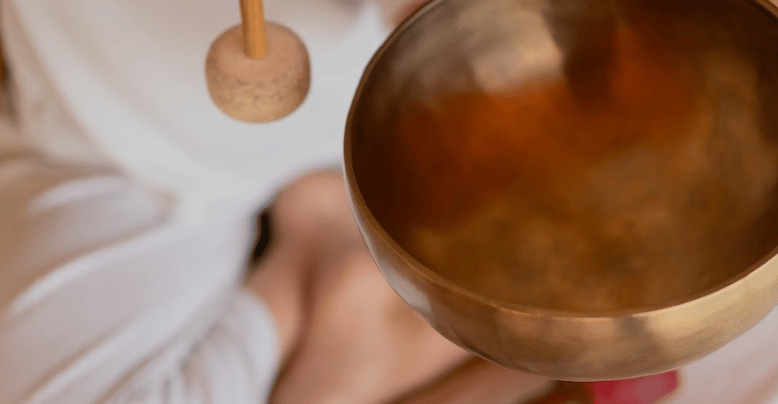 A person using a mallet to play a brass Tibetan singing bowl for sound healing and meditation.