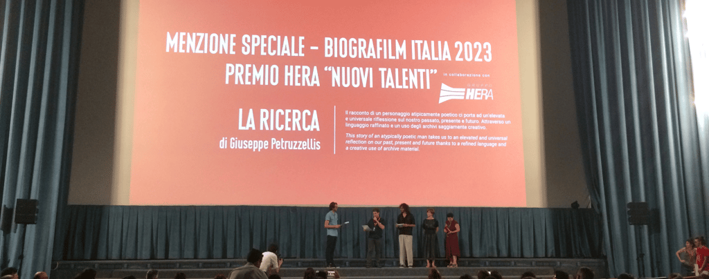 Biografilm Festival 2023 award ceremony for La Ricerca on a large cinema screen with speakers on stage.