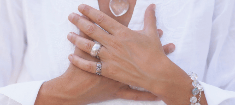 a woman in a white shirt with her hands across her heart wearing silver jewelry