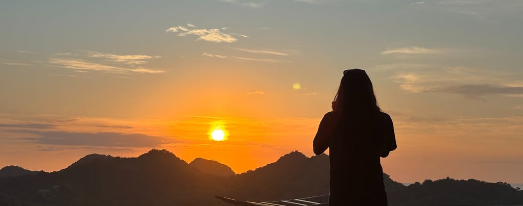 a woman standing on a balcony with a sunset
