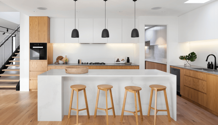 Open-concept kitchen with large island, wooden bar stools, pendant lights, and sleek cabinetry in a modern home