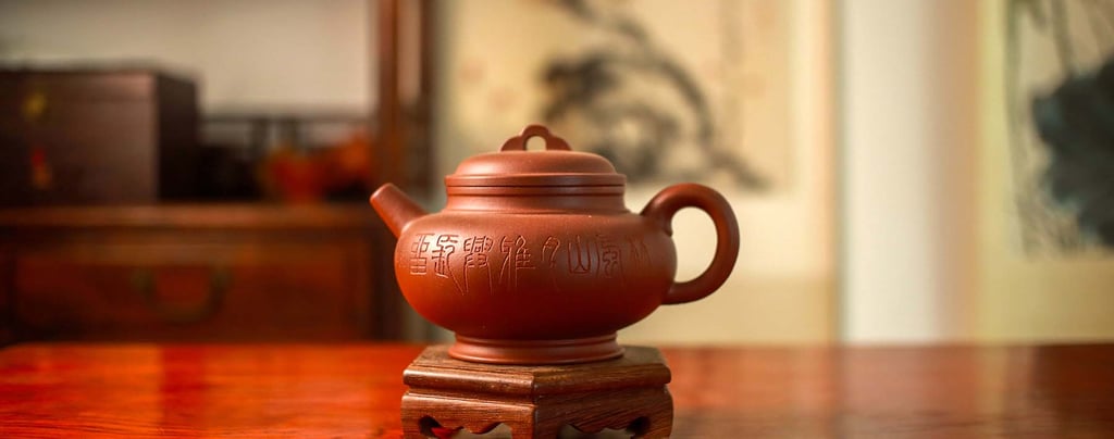A brown Yixing teapot engraved with designs is placed on a wooden stand