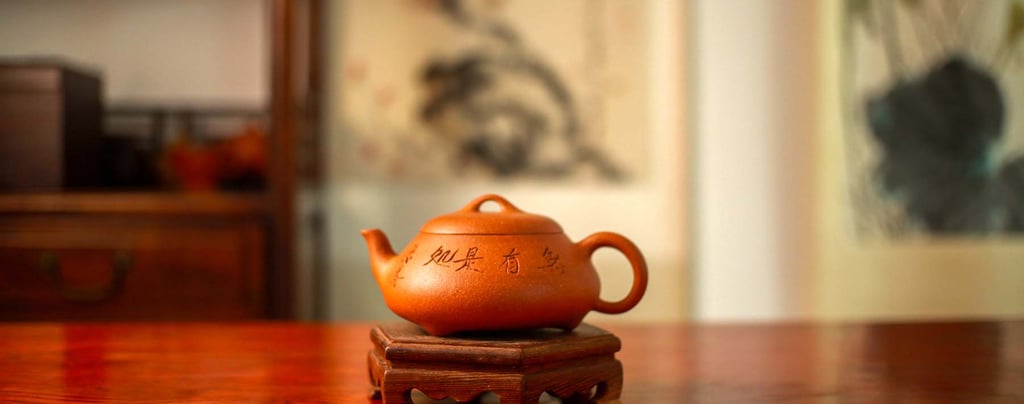 A yellow Yixing teapot engraved with Chinese characters is placed on a wooden stand