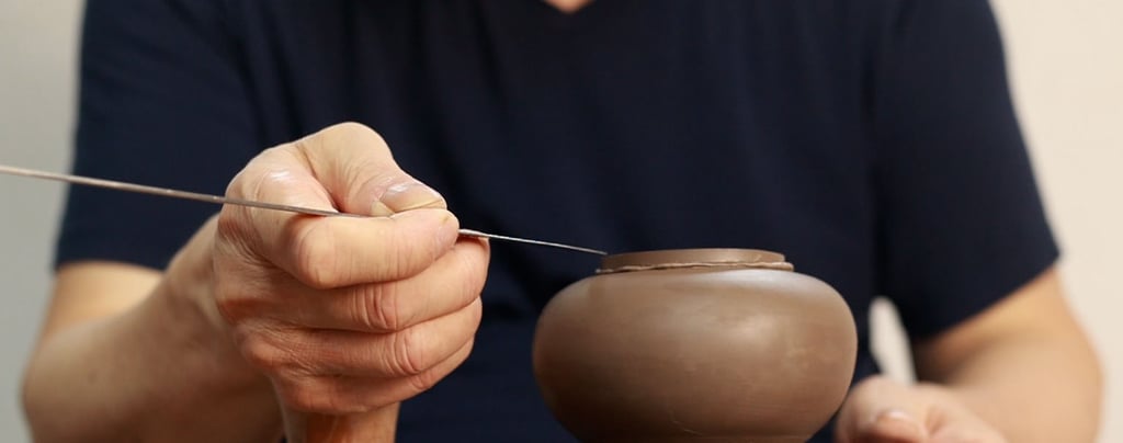 hand holding a long metal knife refining details on a teapot