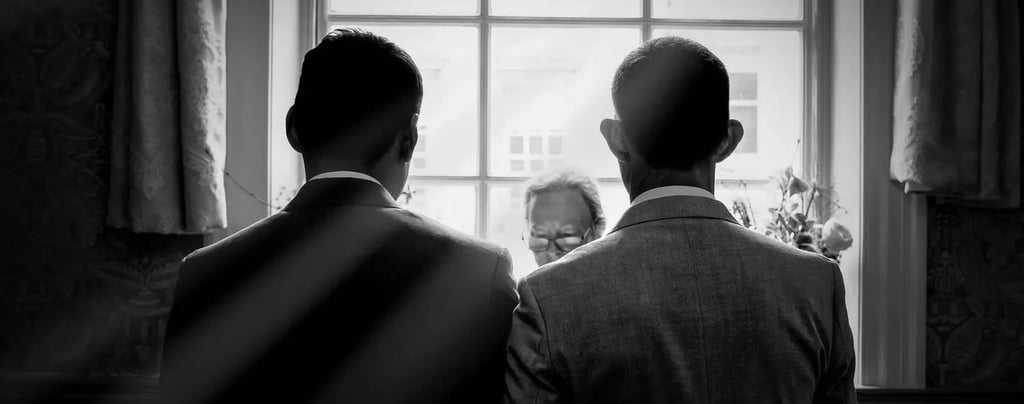 Black and white silhouette of two men in suits at a wedding ceremony standing before an officiant.