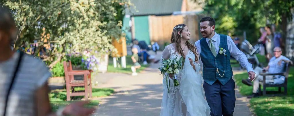 A happy bride and groom walking down a sunny outdoor path at their wedding venue.