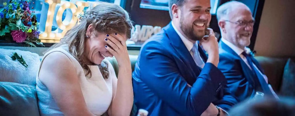 Smiling bride laughing during wedding speeches at her reception dinner.