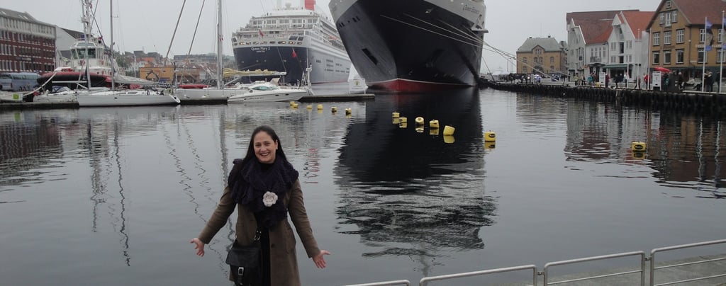 Foto da autora no porto de Stavanger, Noruega — navio Queen Mary ao fundo.