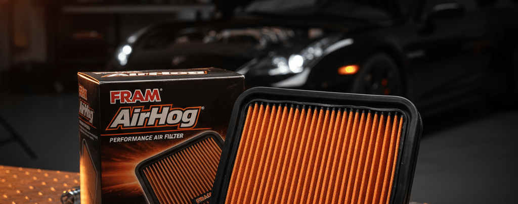 FRAM AirHog performance air filter, orange pleated media, next to its packaging on a metal workbench