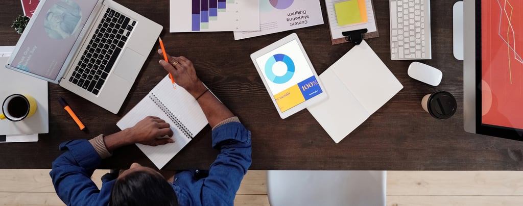 A woman works at her desk, surrounded by papers and devices displaying marketing metrics