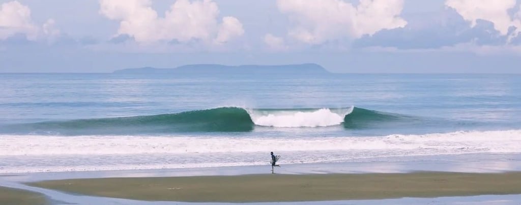 Surfer running on the beach with a perfect wave and an island on the back on a sunny day