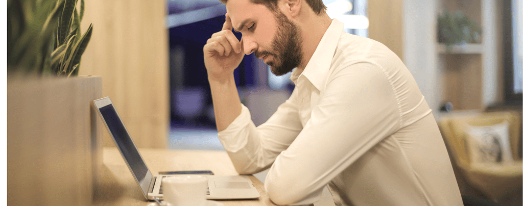 A man sitting thinking at a desk with a laptop computer