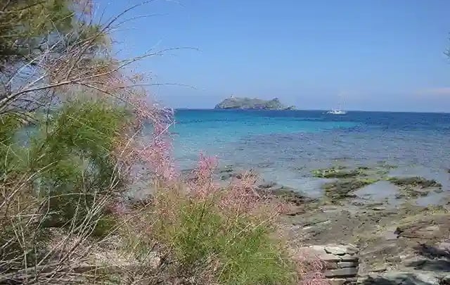 Photo de la mer en Corse d'un bleu intense avec gros rocher au loin et un bateau