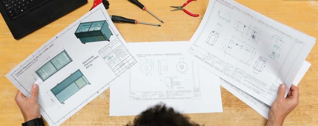 Engineer reviewing technical machine blueprints and CAD drawings at an industrial workstation with tools.