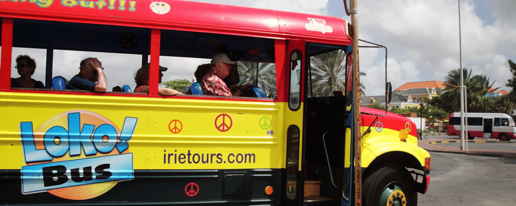 Ônibus turístico colorido circulando pelas ruas de Willemstad, Curaçao, oferecendo passeios.