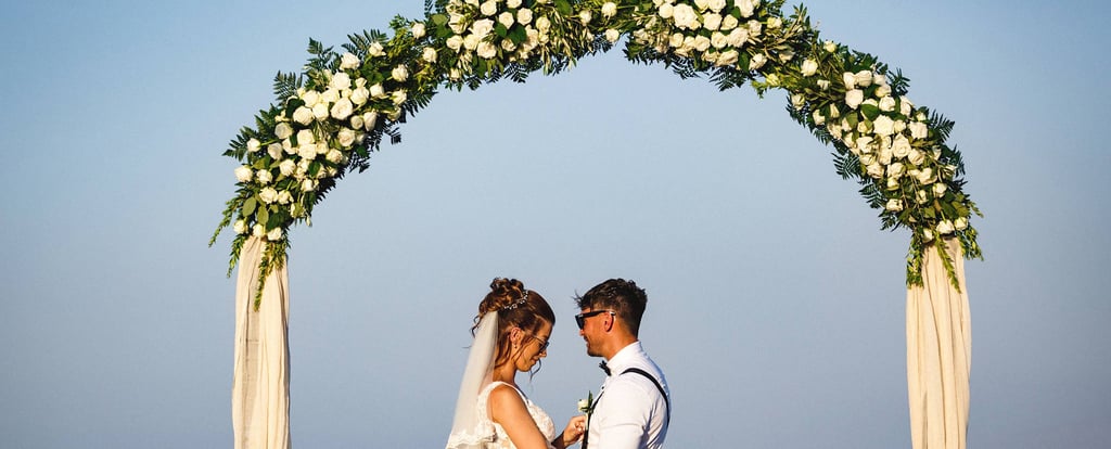 gli sposi dopo la cerimonia, abbracciati sotto un arco floreale di rose bianche che decorava il luogo della cerimonia