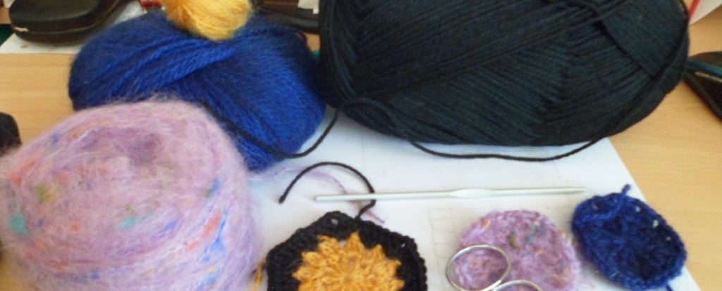 Pelotes de laines posées sur une feuille blanche qui est posé sur une table un crochet au milieu