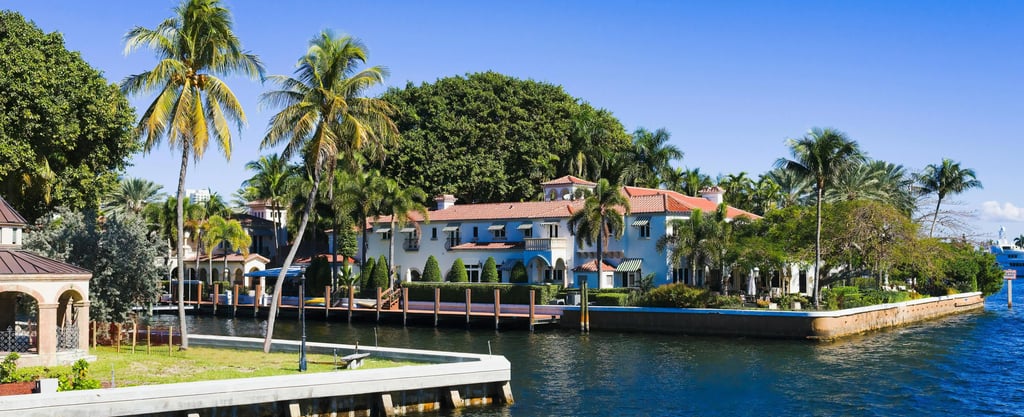 Luxury waterfront mansion in Miami with palm trees, a private dock, and Mediterranean architecture.