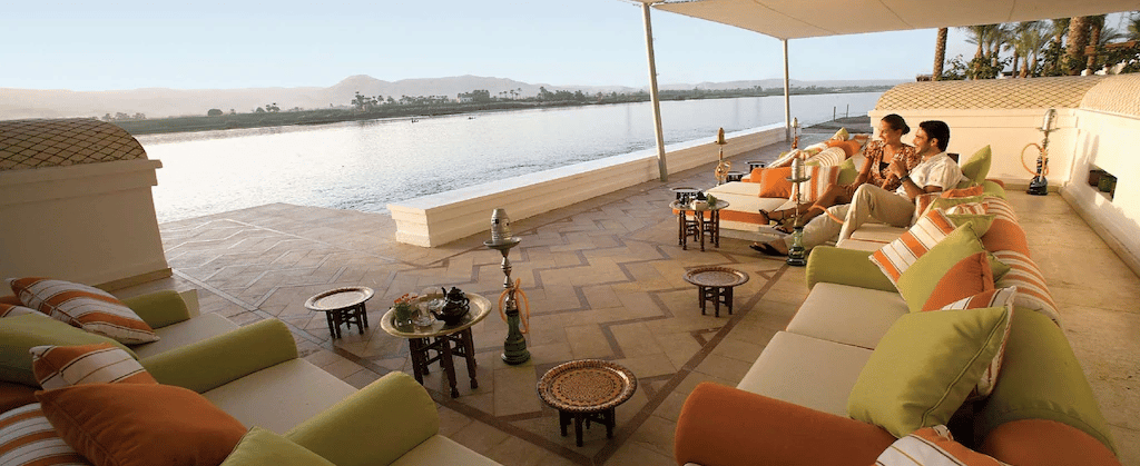 Couple relaxing at Hilton Luxor Resort & Spa terrace with outdoor sofas and shisha pipes.