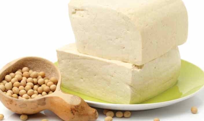 two blocks of tofu staked and a wooden spoon with soya beans