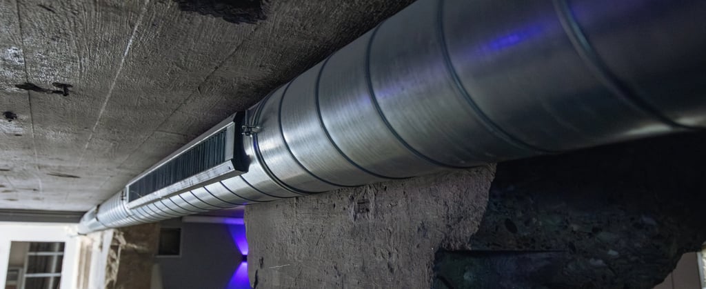 Industrial spiral ductwork and ventilation grille installed against a concrete ceiling in a modern basement.