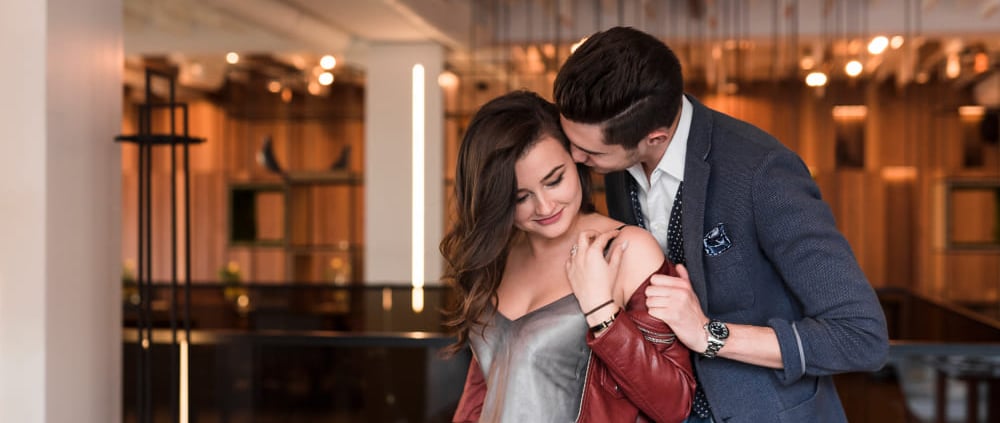 A sugar mommy in an elegant dress embracing her sugar baby in a luxurious restaurant.