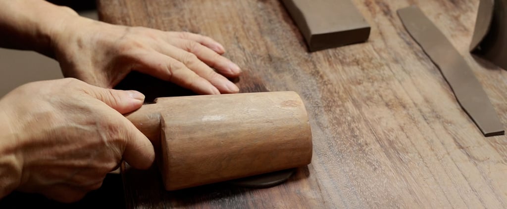 A person using a wooden tool to pound clay, with more clay nearby