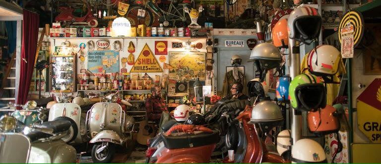 Vintage scooter repair shop filled with classic Vespas, retro helmets, and antique oil signage.