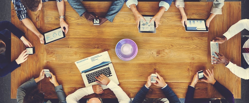Overhead view of a diverse business team analyzing data on digital tablets and laptops around a wooden table.