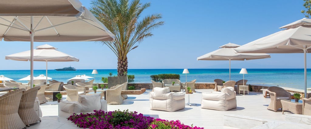 Sani beach hotel white umbrellas, and palm trees overlooking the turquoise sea.