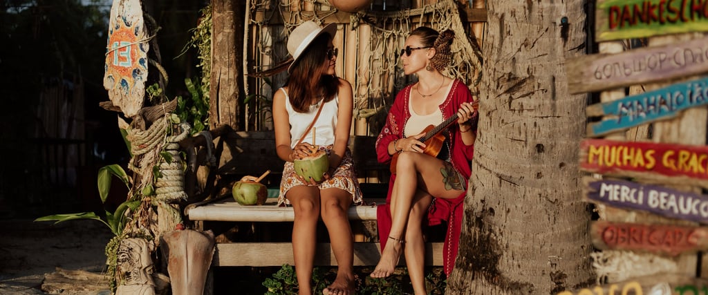 Two women relaxing at a tropical beach bar, drinking fresh coconut and playing ukulele at sunset.