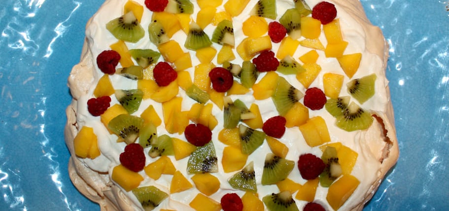 pavlova decorated with kiwi, raspberries and mango