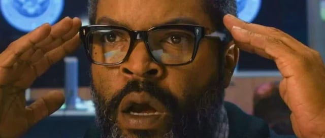 Ice Cube with a shocked expression and hands raised to his head, reacting to intense news in a scene