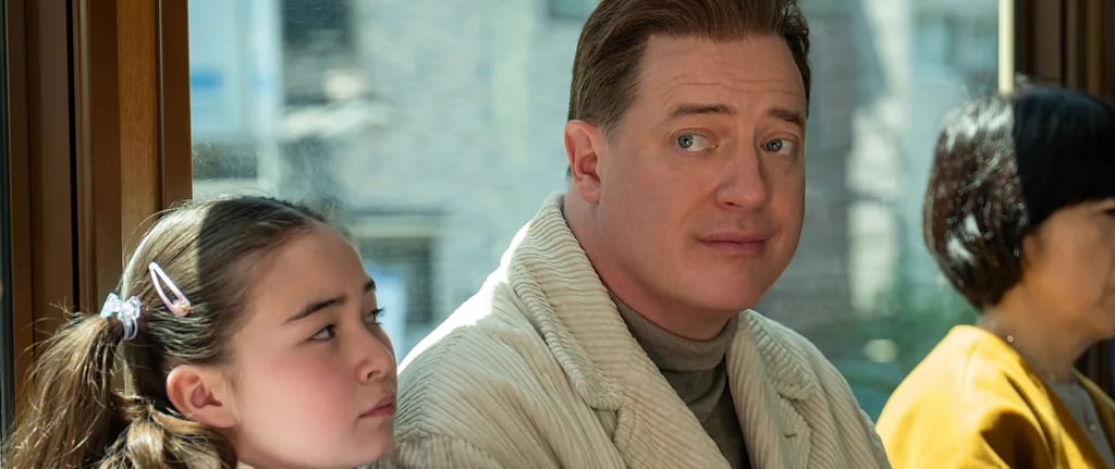 Brendan Fraser sitting beside a young girl, glancing over his shoulder with a subtle expression — sc