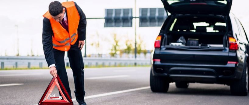 Un homme en gilet de sécurité se tient à côté d'une voiture en panne.
