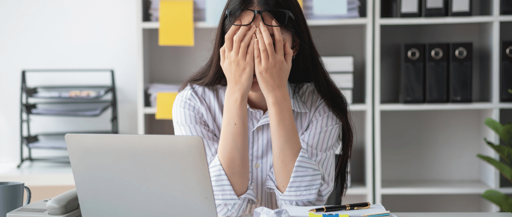 a woman sitting at a desk with her hands covering her face