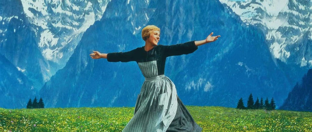 Julie Andrews as Maria stands arms wide on a mountain in The Sound of Music