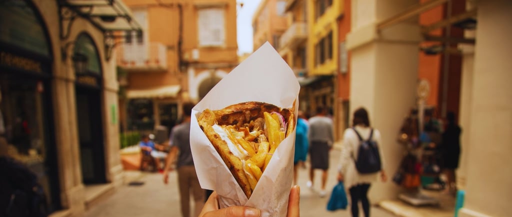 Autora segurando um gyros enquanto caminha pelas ruelas movimentadas de Corfu, explorando a cidade.