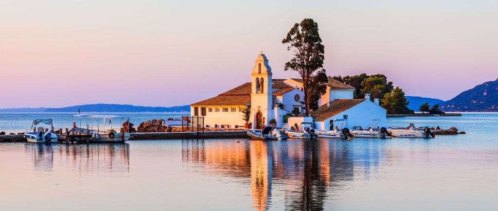 Vista do passeio de barco em Corfu, com a igreja no mar ao fundo e barcos ancorados no pier.