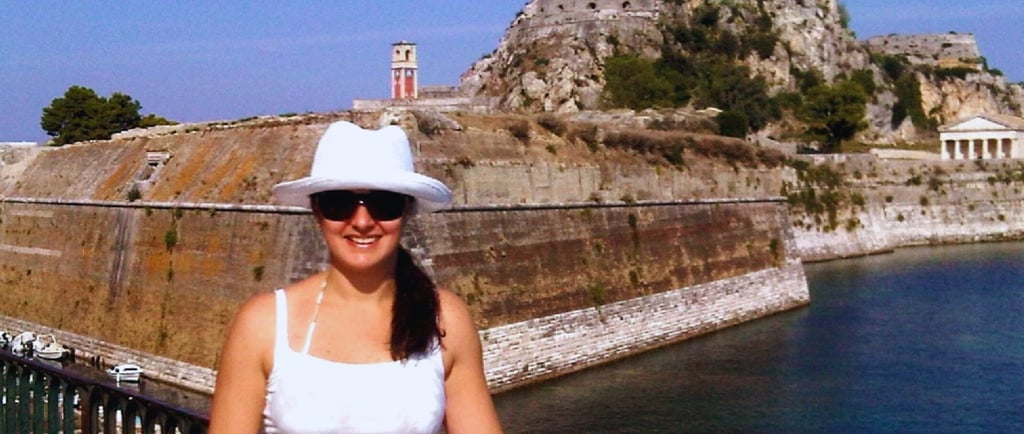 Autora diante da Fortaleza Antiga de Corfu, com a imponente estrutura histórica ao fundo.