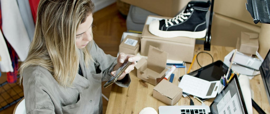 Woman with laptop taking photo of boot to sell surrounded by boxes