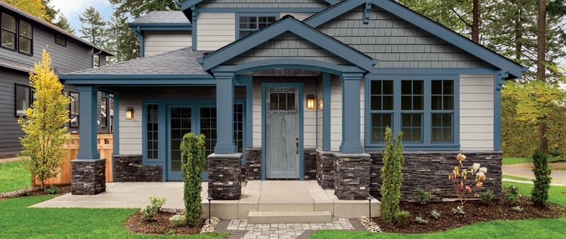 A beautifully painted two-story home with blue and gray exterior tones, stone accents, and a welcom