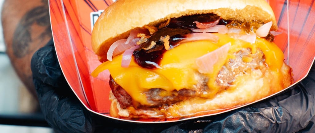 a man holding a large hamburger burger on a paper plate
