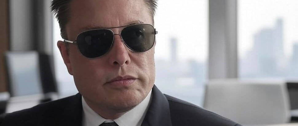 a man in a suit and sunglasses sitting at a table